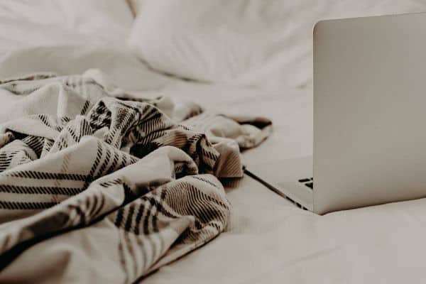 laptop on a bed with a throw blanket next to it