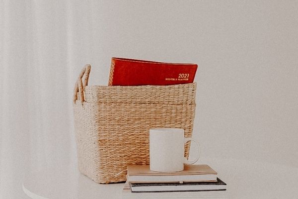 Baskets with a planner sitting inside, with a coffee cup sitting on notebooks