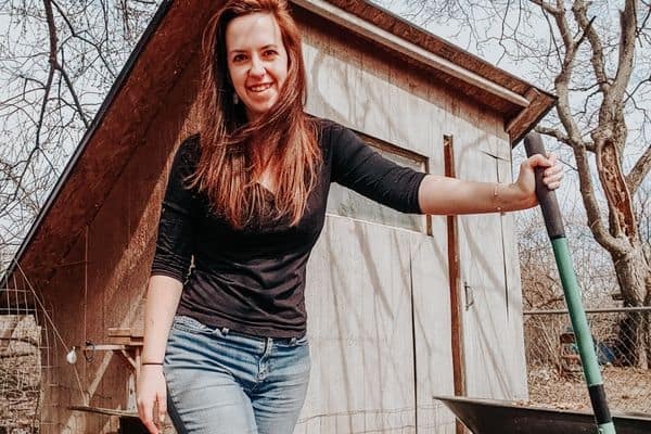 leah lynch standing in front of a chicken coop holding a shovel
