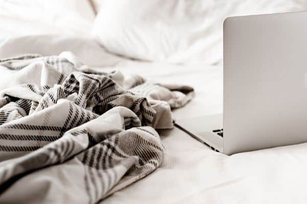 laptop on a bed with a cozy blanket close by